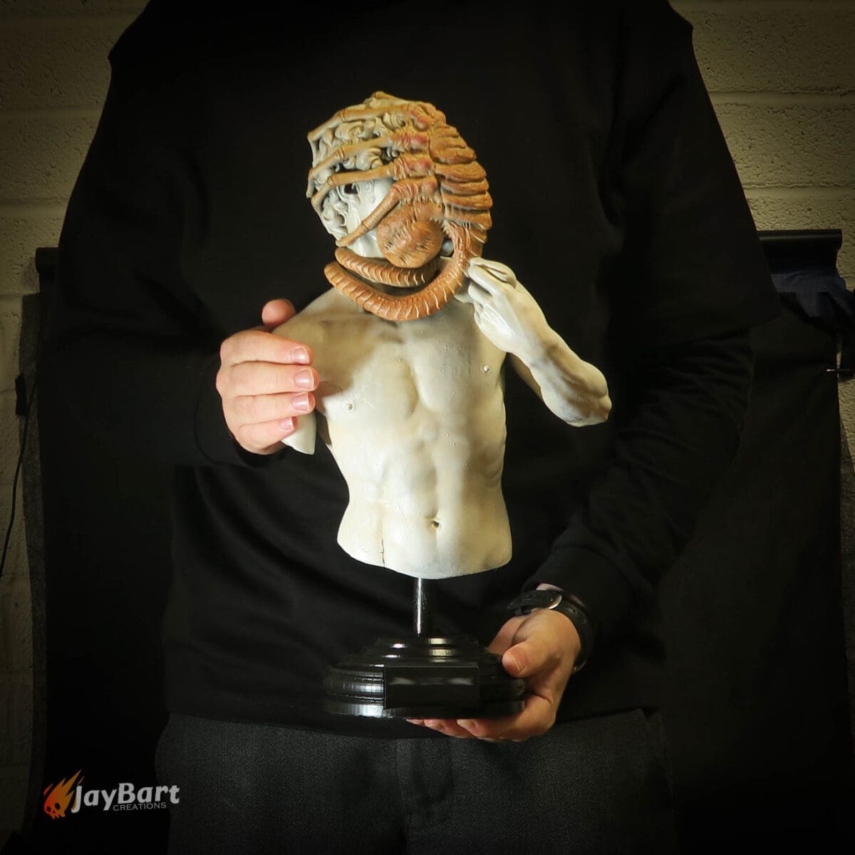 Person holding sculpted torso with intricate headpiece.
