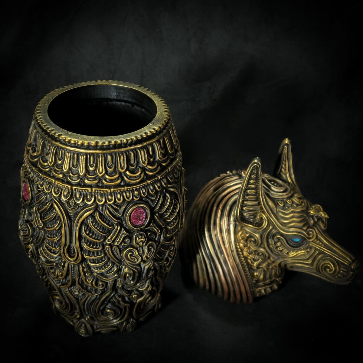 Ornate gold urn and Anubis head sculpture on black background.