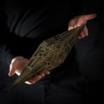 Person holding a geometric, bronze-colored object.