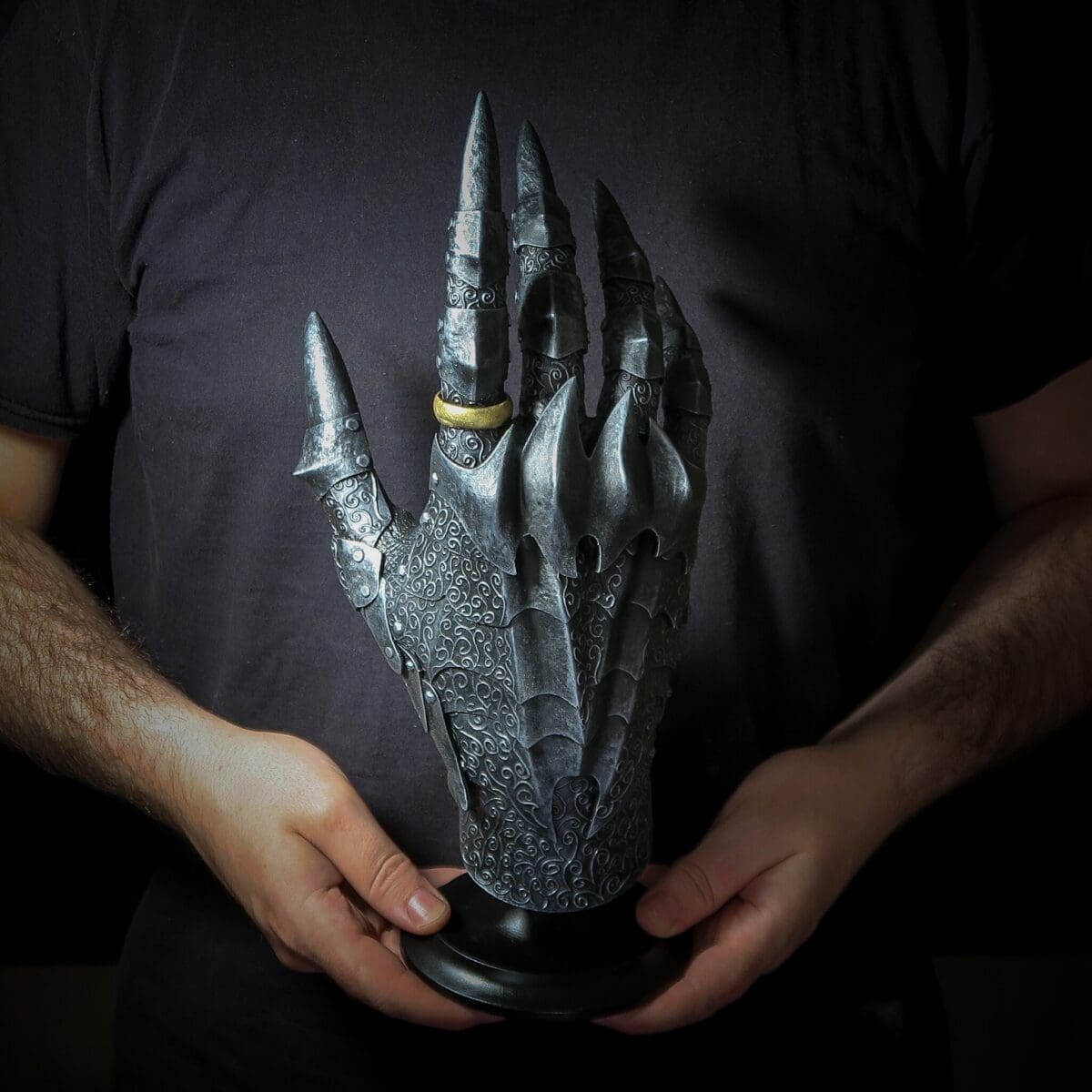 Sculpture of armored hand with ring, held by person.