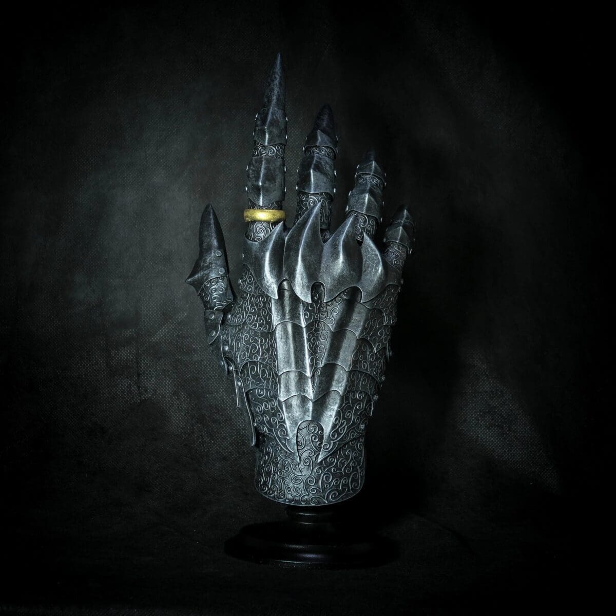 Ornate medieval gauntlet with gold ring on dark background.