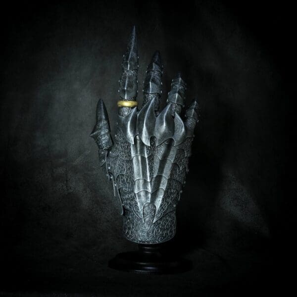 Ornate medieval gauntlet with gold ring on dark background.