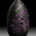 Black vase with purple flowers and gold cracks.