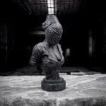 Creepy faceless sculpture in dark, eerie room.